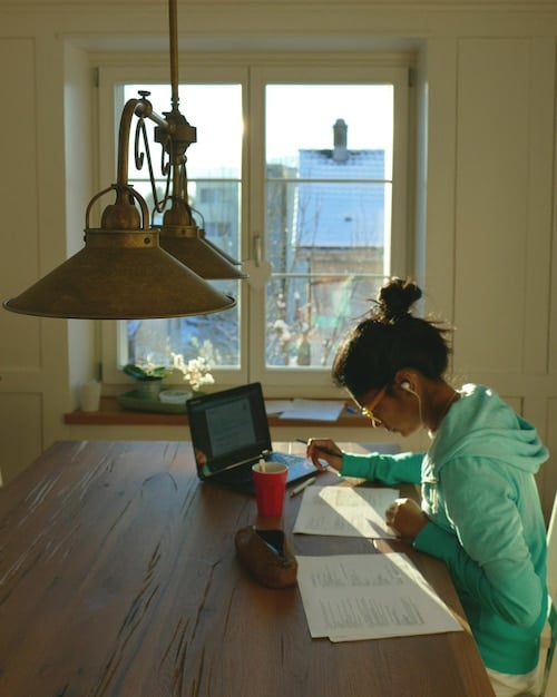 A person using a laptop to review tax documents and financial statements in a home office setting. Natural light fills the room, highlighting the organized workspace.