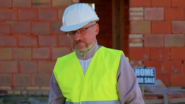 A zoomed-in shot of a construction worker wearing a yellow helmet, blue t-shirt and jeans working at a construction site.