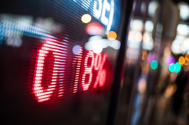 Image of a digital stock ticker displaying red numbers, symbolizing a market downturn, with blurred city background.